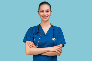 Studio portrait of a young brunette doctor woman in surgical uniform posing over light blue background