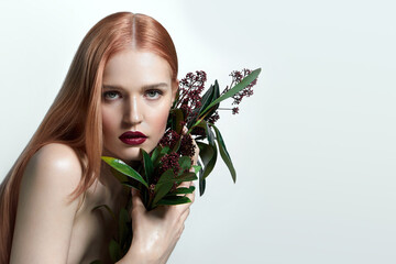 Portrait of a beautiful young woman with red hair. A bouquet of red flowers in the hands. Light, smooth, well-groomed skin. Advertising of cosmetics.