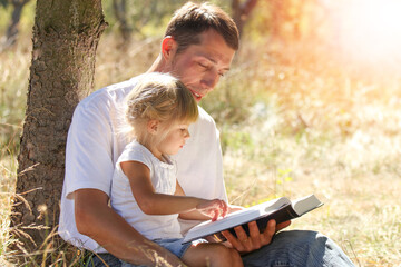 Happy parents with a child read the Bible in the nature park