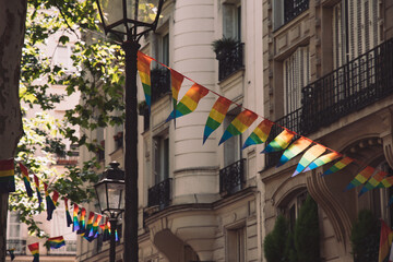 Decoration of triangle shape banners in colors of Lgbtq flags hanging between vintage lantern streetlights and ornate stone house with balconies. Gay pride parade in Paris France