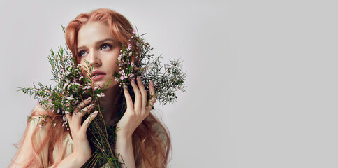 Portrait of a beautiful young woman with red hair and flowers near the face.