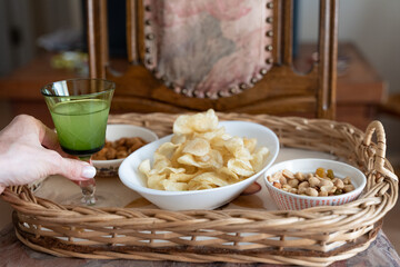 Hand of woman taking pisco sour glass on tray with chips and dried fruits and nuts. Snack time concept