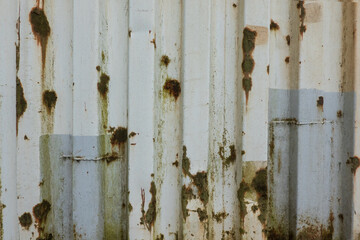 Fragment of the wall of an old white metal shipping container. On the profiled surface there are traces of repair and corrosion centers. Background. Texture.