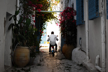 Motorcyclist rides down a narrow street. View of the old cute street with flowers. Retro italian moped.