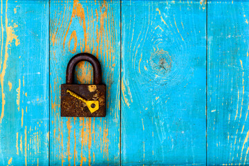 Ancient and rusty closed padlock with key on old wooden table covered with blue paint. View from above