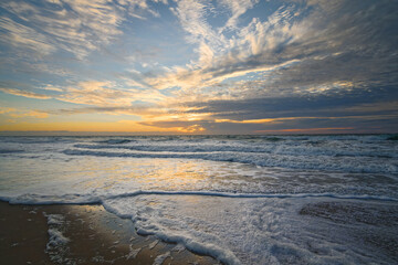 Tropical beach sunset. Empty sand beach, beautiful cloudy sky, and sea waves breaking the shore