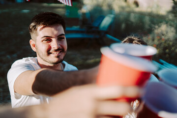 Chico brindando con vasos rojos con amigos en una barbacoa por el dia 4 de julio día de la independencia  de estados unidos