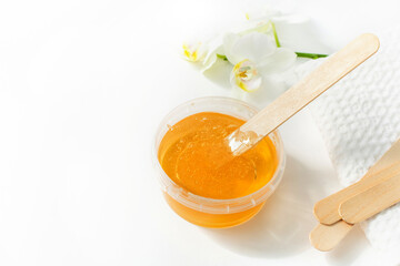 Sugar paste or wax honey in a transparent jar and white orchid on a white background. Sugaring. Depilation and beauty concept. Waxing.