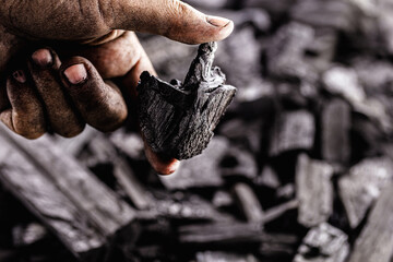 hand holding piece of charcoal, with background. Dirty coal emitter hand