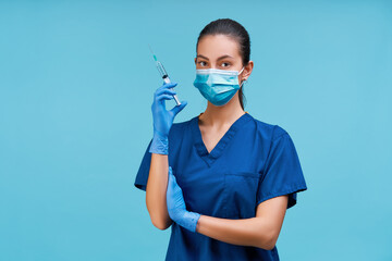 Studio shot of confident young woman doctor wearing protective mask and rubber gloves holding syring vith vaccine in her hand