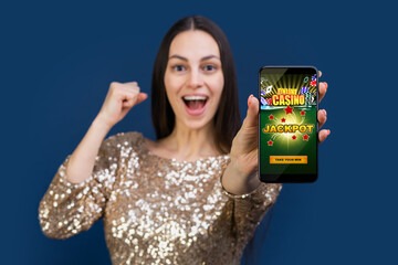 Happy woman in sparkling dress showing smartphone screen with online casino website interface to the camera and clenching fist in winner gesture - 433511606
