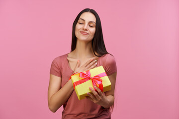 Young casually dressed pretty woman accepting a present with grateful face expression and gesture, isolated over pastel pink background
