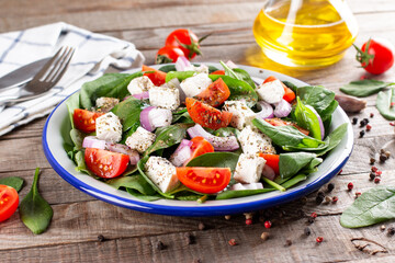 Healthy food. Greek salad with spinach, tomato, sweet pepper, red onion, feta cheese on a wooden table.