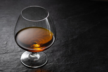 Amber brandy in cognac glass on black stone table with studio reflection