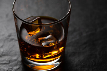 Amber whiskey with ice cubes in the old fashion glass on black stone table with studio reflection. close up view