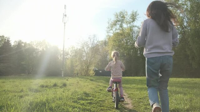 Mom teaches the child to ride a bicycle, pna path in the park, helps not to fall. The child goes by himself