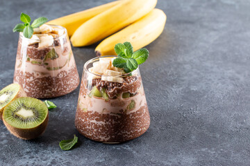 Cocoa chia seed pudding with kiwi and banana on dark gray table. Healthy vegan breakfast, copy space.