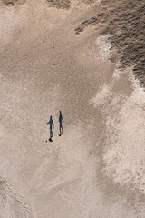 Aerial top-down picture featuring two persons going across a dry desert surface of a salt lake casting long shadows in the low morning sun