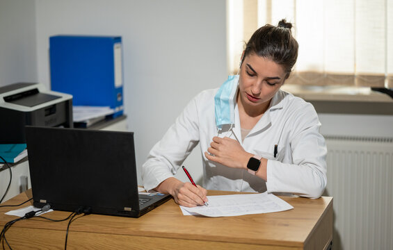 Portrait of a tired woman doctor sitting on her desk and writing on paper.
