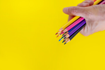 A hand holding some coloured pencils, isolated on a yellow background