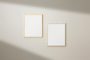 Set of two frames mockup. Thin wood frames hanging on a neutral coloured. Window light creating long shadows.