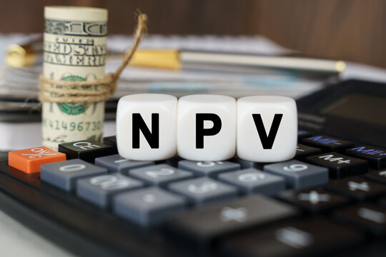There are cubes on the calculator that say - NPV. Nearby out of focus - dollars, notebook and pen