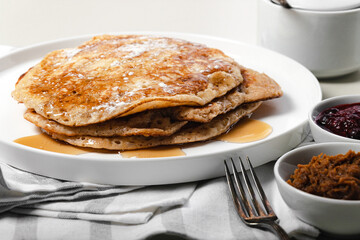 Delicious hot pancakes with maple syrup. Traditional delicious dessert or sweet breakfast on a white plate on a light table. Forks, striped napkin and white dishes.