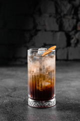 Cocktail in glass with cola, alcohol, ice, decorated dried orange on gray background.