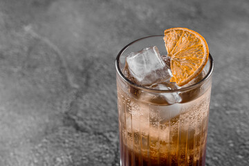 Cocktail in glass with cola, alcohol, ice, decorated dried orange on gray background.