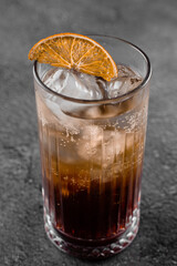 Cocktail in glass with cola, alcohol, ice, decorated dried orange on gray background.