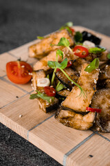 Fried eggplants on a wooden board, decorated with chili, garlic, cilantro, sesame seeds on a gray background.