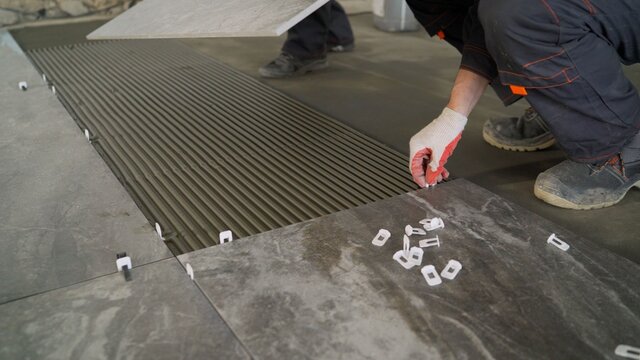 Adhesive solution for gluing ceramic floor tiles. Professional worker gluing decorative tiles to the floor. Industrial scale mortar application for gluing tiles to floors.