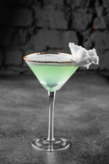 Green alcohol cocktail in a glass decorated with cotton candy on gray background.