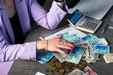 Female manicured hands with red nail polish reach for a heap of money. Dollars, british pounds...