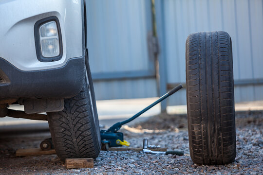 Car standing on jack-screw for snow tire removing, summer wheel is ready to install