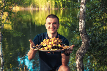Happy welcoming smiling man greets guests with a freshly prepared barbecue dish of grilled...