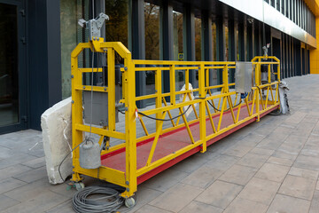Suspended construction cradle after glazing the facade of a commercial object stands on the ground....