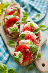 Caprese open faced sandwich based on sourdough bread with the addition of tomatoes, mozzarella cheese, fresh basil and olive oil on a white board close up view