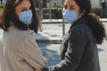 two businesswomen with blue surgical face masks together looking back outdoors in street