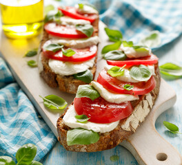 Caprese open faced sandwich based on sourdough bread with the addition of tomatoes, mozzarella cheese, fresh basil and olive oil on a white board close up view
