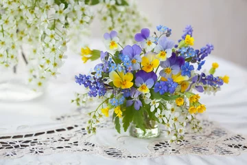 Fotobehang A bouquet of spring blue, yellow flowers in a vase on the table. Pansies, forget-me-nots, primroses, bird cherry, violets, muscari. Postcard, blur, selective focus. © tachinskamarina