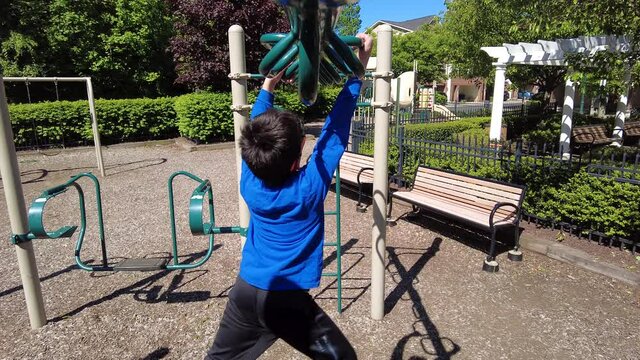 A boy  is moving across a series of monkey bars at a playground. Concept footage for activity, exercise, childhood, physical activity, development and urban, residential neighborhood playgrounds.