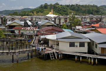 Fototapeta na wymiar A gold-domed mosque rises behind houses on stilts in the Kampung Ayer water village on the Brunei River in Bandar Seri Begawan, Sultanate of Brunei