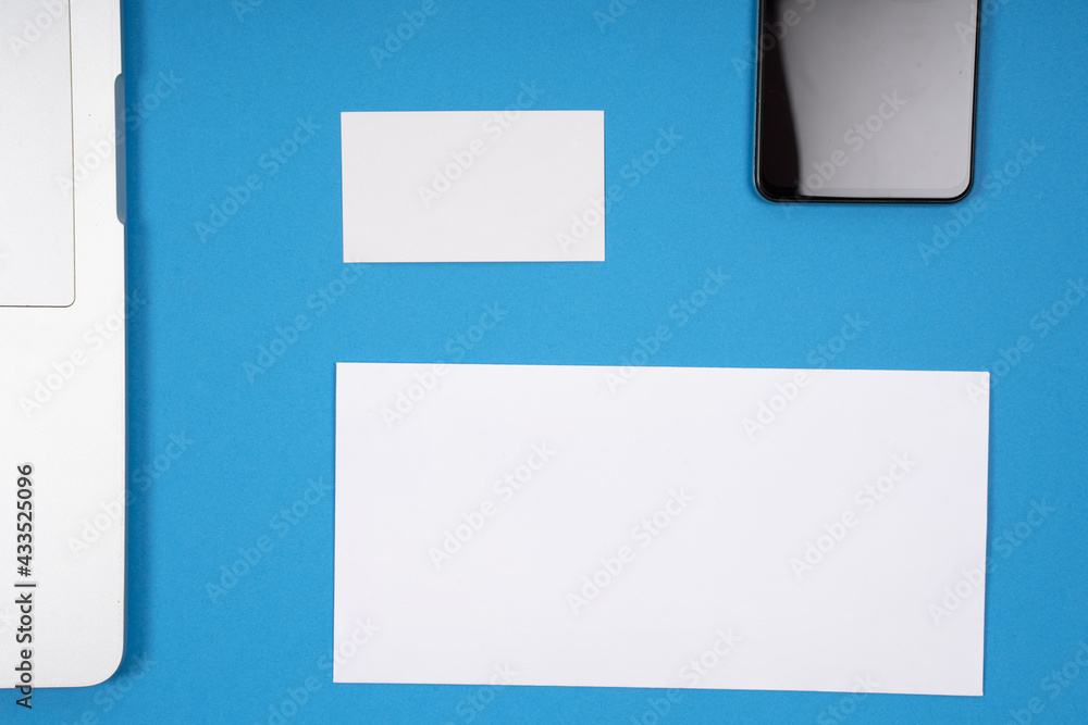 Poster top view of a laptop and a smartphone with blank pieces of paper for your text on blue background