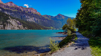Fototapeta na wymiar Swiss alps in background with blue turquoise lake in foreground and gravel path leading towards water, Alpines in Switzerland, holiday and vacation area