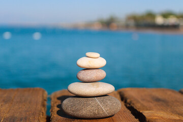 Pyramid of stones on a wooden pier by the sea. Zen concept. Blurred background. Concept of harmony, stability, life balance, and meditation. Summer mood
