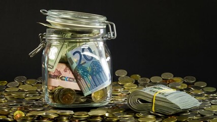 Glass tip jar with dollar, euro and ruble bills rotation in a heap of coins 4K