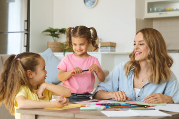 Young beautiful woman mother drawing with colorful pencils with her two cute little kids sisters siblings, family of mom and daughters playing together during self isolation and covid 19 outbreak