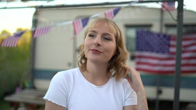 Chica rubia joven delante de una caravana con bandera de estados unidos sonriendo