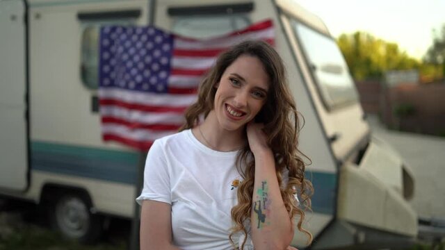 Chica joven con top blanco y bandera de estados unidos frente a una caravana 